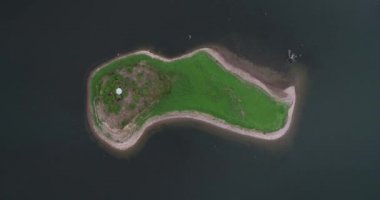 Senital havadan insansız hava aracı sahnesi mavi gölde küçük yalnız yeşil adaya doğru iniyor. Cabra Corral Barajı'ndaki ıssız ada, Salta'nın turistik alanı, Arjantin