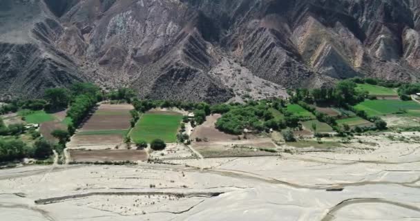 Scène aérienne de drone de petite agriculture locale entre la vallée de la rivière et la pente colorée désertique. Paleta del Pintor, Maimara, Jujuy, Argentine — Video