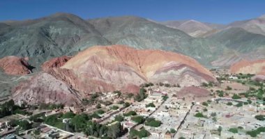 Geriye doğru hareket eden hava drone sahnesi, renkli kuru dağlarla çevrili köyün panoramik manzarasını gösteriyor. Yedi renk dağlar, Purmamarca kasaba Jujuy, Arjantin. Turistik bir şehir. Cerro siete renk