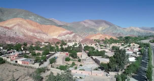 Antena Drone sceny rosnąco pokazując panoramiczny widok na wioskę otoczoną barwnie erozji gór. Siedem kolorów gór, Purmamarca miasto, Jujuy, Argentyna. Turystyczne miasto. Cerro Siete Colores — Wideo stockowe