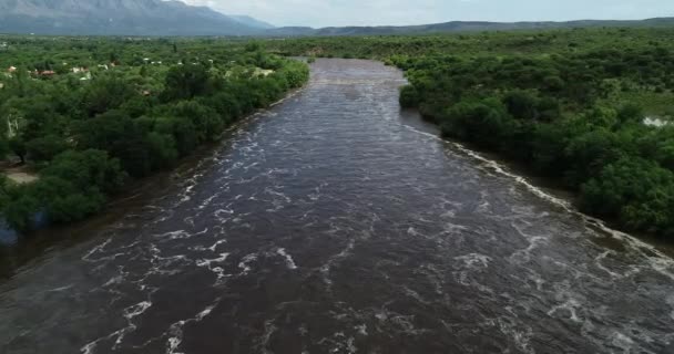 La scena aerea del drone sorvola il forte fiume marrone che passa sul ponte. Alluvione a Mina Clavero. Fiume in crescita sulle strade della città. Cordoba, Argentina — Video Stock