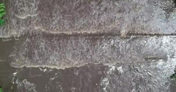 Escena aérea senital de puente inundado, agua fangosa marrón que pasa sobre la construcción. Ascendiendo desde el detalle del agua hasta la vista general del puente y las calles. Mina clavero, traslasierra, cordoba argentina — Vídeo de stock