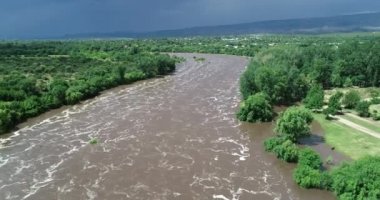 Güçlü köpüklü kahverengi nehrin üzerinde uçan hava aracı sahnesi. Kasaba arka planda. Mina Clavero 'da sel. Şehrin sokaklarında büyüyen nehir. Cordoba, Arjantin