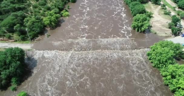 Scena aerea drone del fiume Brown che passa, allagamento, ponte. Volare sopra il fiume muovendosi verso l'alto. Acqua turbolenta, cambiamenti climatici. Mina clavero, Cordoba, Argentina — Video Stock