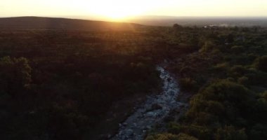 Dağ nehri ve odunsu arazinin üzerinde altın günbatımının hava aracı görüntüsü. Arka planda dağlar ve güneş. San Javier, Cordoba, Arjantin 'de altın saat