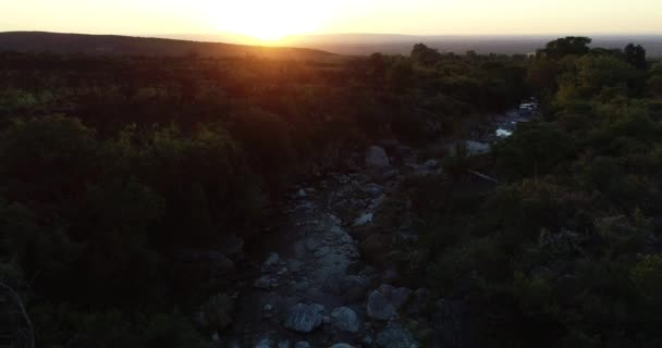 Espectáculo aéreo seco de puesta de sol naranja sobre el río rocoso de montaña entre el paisaje de woody. Montañas y sol en segundo plano. Hora de oro en San Javier, Córdoba, Argentina — Vídeos de Stock