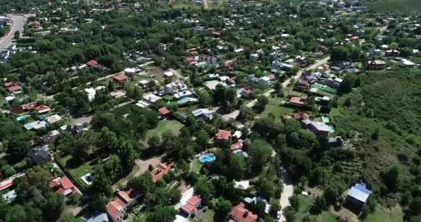 Панорамный вид с воздуха на туристический город с зелеными насаждениями. Жилые дома между зелеными пейзажами. Потреро-де-лос-Фунес, Сан-Луис, Аргентина — стоковое видео
