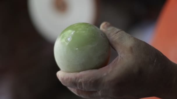 Plan au ralenti de l'homme montrant une sphère verte semi-précieuse polie. Gros plan des mains, disque blanc tournant à l'arrière-plan. Décoration artisanale. La Toma, San Luis, Argentine — Video