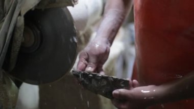 Yarı değerli taşla çalışan bir adamın yavaş çekim görüntüsü. Stromatolit kaya fosilini kesip disk ve su keserek mücevher yaratmak için ellerinizi kapatın. La Toma, San Luis, Arjantin