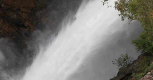 Água caindo com força contra a bacia rochosa espirrando vapor de água em penhasco de rocha. Cachoeira. Vegetação e estruturas rochosas em primeiro plano. Córdoba, Argentina — Vídeo de Stock