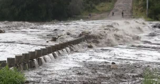 Silna rzeka przechodząca przez most. Burzliwy gwałtowny przepływ wody nad budową. Ludzie i ogrodzenie po drugiej stronie rzeki w tle. Powódź w Mina Clavero, rzeka uprawna, Cordoba, Argentyna — Wideo stockowe