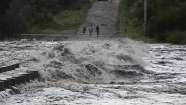 Powolny ruch silnej gwałtownej rzeki przechodzącej przez most, budowa. Ludzie i ogrodzenie po drugiej stronie rzeki w tle. Powódź w Mina Clavero, rzeka uprawna, Cordoba, Argentyna — Wideo stockowe