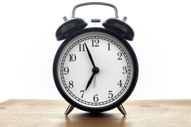 Beyaz arkaplanda izole edilmiş ahşap masa üzerindeki klasik siyah alarm saati