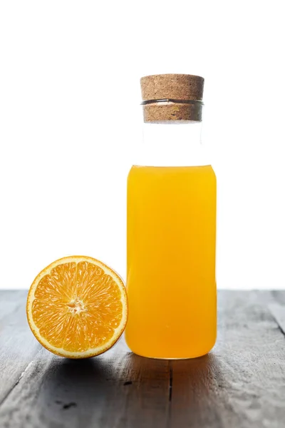 a glass bottle of fresh and cool orange juice with fresh half orange fruit on a table isolated on a white background