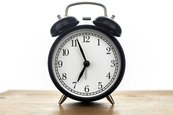 Beyaz arkaplanda izole edilmiş ahşap masa üzerindeki klasik siyah alarm saati