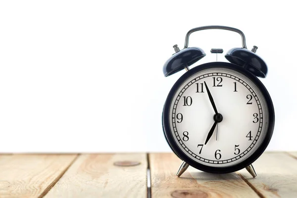 Beyaz arkaplanda izole edilmiş ahşap masa üzerindeki klasik siyah alarm saati
