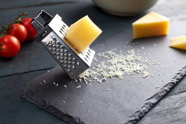 Parça ve rendelenmiş parmesan peyniri siyah servis tahtasının üzerinde kiraz domatesli ahşap masada. Salata serpmek için rendelenmiş parmesan..