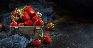 Koyu ahşap bir masa üzerinde bir kutu içinde çilek