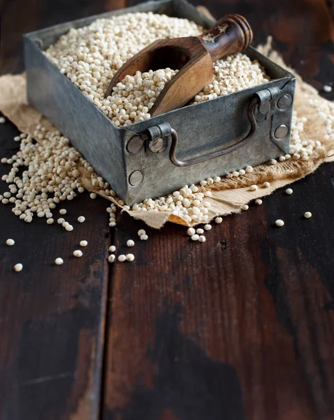 暗い木製のテーブル上の金属製のボックスで生白ソルガムの穀物 — ストック写真