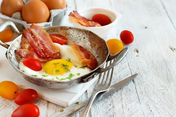 Breakfast with fried eggs and bacon in an old frying pan