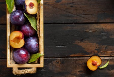 Bir kutu içinde yapraklarda bir ahşap masa üstü ile taze erik görüntülemek