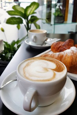 Kafedeki siyah masada ayçöreği olan bir fincan cappucino.