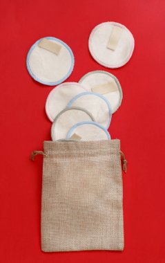 Eco friendly reusable make-up remover pads in bag on red  background top view clipart