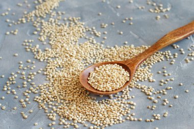Gri bir masada, bir kaşık çiğ beyaz kinoa tohumu yakın plan.