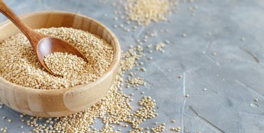 Bir kase çiğ beyaz kinoa tohumu ve gri bir masada kaşık.