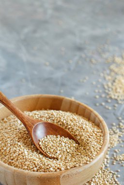 Bir kase çiğ beyaz kinoa tohumu ve gri bir masada kaşık.