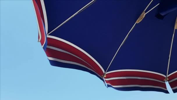 Close-up of blue, white and red beach umbrella against the blue sky — Stock Video