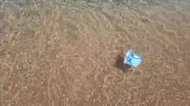Bir kişi denize atılmış yüz maskesini çıkarıyor..