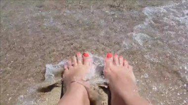 Bronzlaşmış kadın ayaklarının üzerinde süzülen deniz dalgaları