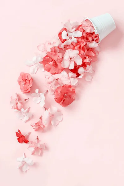 Flowers fall down of a white bucket on light pink background top view