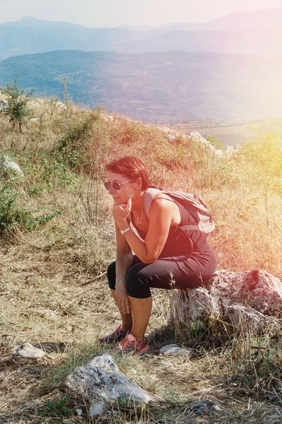 Female hiker takes a break in mountains in a sunny  day