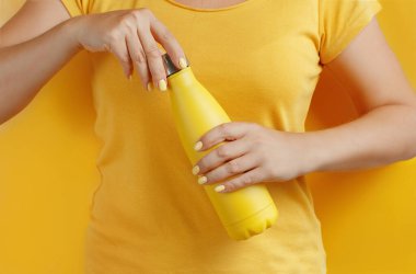 Sarı arka planda sarıyı tekrar kullanılabilir şişeyi tutan kadına yaklaş. 