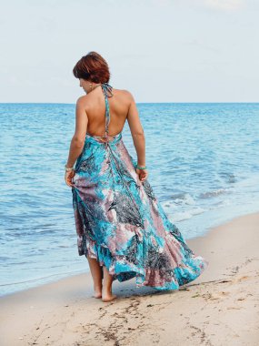 Kumsalda yürüyen uzun elbiseli genç kadın.