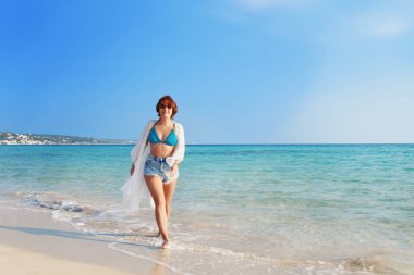 Giyinik genç bir kadın ve kumsalda yürüyen kot şortlu bir kadın. Seyahat ve tatil kavramı.