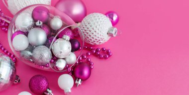 Pembe arka planda şarap kadehinde Noel mücevherleri.