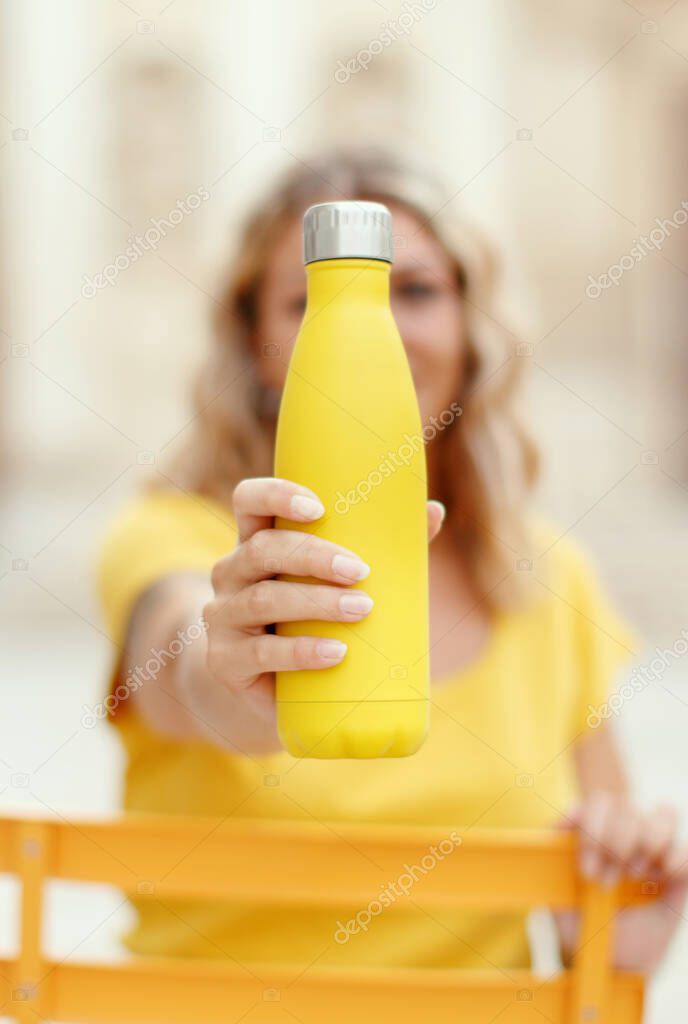 Young woman in yellow t-shirt holding yellow reusable bottle  selective focus
