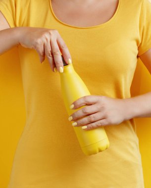 Sarı arka planda sarıyı tekrar kullanılabilir şişeyi tutan kadına yaklaş. 