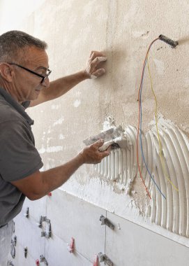 Usta bir zanaatkar fayans yapıştırıcısını fayanssız bir duvar yüzeyine serpiştirir, yakın plan. Yeni bina inşaatı veya yenilenmesi. 