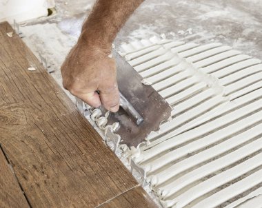 Zanaatkar fayans yapıştırıcısını fayanssız bir evin zeminine serpiştirir, eller yakın çekim yapar. Yeni bina inşaatı veya tadilatı. Porselen taş savaşıyla döşeme