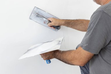 Tozlu zanaatkar, odanın içindeki duvarın kaymağını sıyırmak için mala ve şahin kullanır. Bir evin inşaatı veya tadilatı sırasında gri iş elbiseli adamlar, DIY ev geliştirme