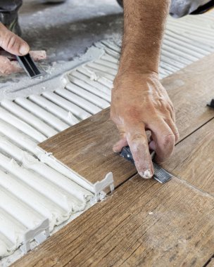 Tiler yere porselen döşemeler yerleştirmek için boşluk kullanıyor. Yapışkan ve kirli ellerle hazırlanmış. Bir evin inşaatında ya da yenilenmesinde çalışan zanaatkar, DIY ev imalatçıları