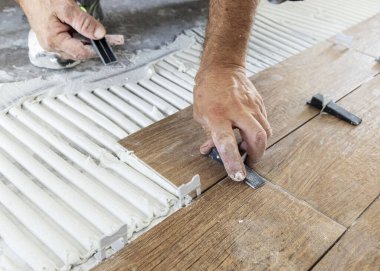 Tiler yere porselen döşemeler yerleştirmek için boşluk kullanıyor. Yapışkan ve kirli ellerle hazırlanmış. Bir evin inşaatında ya da yenilenmesinde çalışan zanaatkar, DIY ev imalatçıları