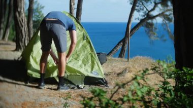 erkek bir turist bir çadır pine Grove dik kıyı kıyı kenarında deniz manzarası muhteşem bir görünüm ile düzenler. 4k.
