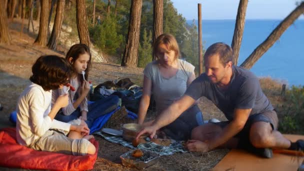 Egy boldog család mellett egy sátor, a szélén egy meredek tengerparton, egy fenyőligetben csodálatos kilátás nyílik a seascape kemping étkezés, a turisták. 4k. — Stock videók