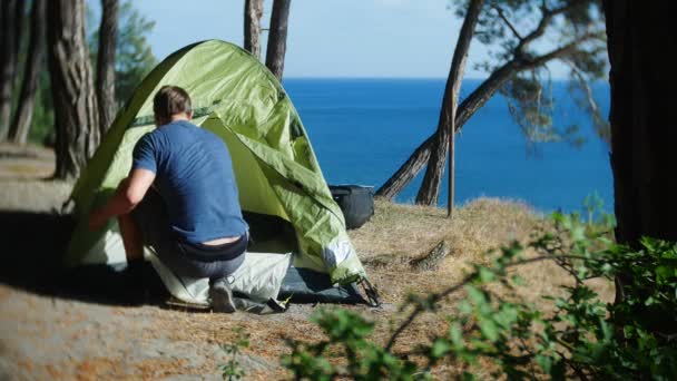 Manliga turist arrangerar ett tält i utkanten av en brant kust strand i en pinjelund med en magnifik utsikt över marinmålning. 4k. — Stockvideo