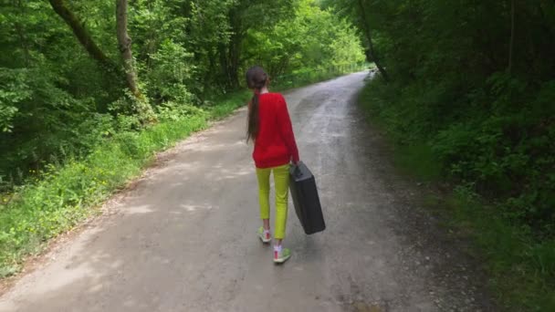 Дівчина, гуляє по лісу з важкою чорною валізою. 4k, стрільба з повільним ходом, стрільба зі стайні . — стокове відео
